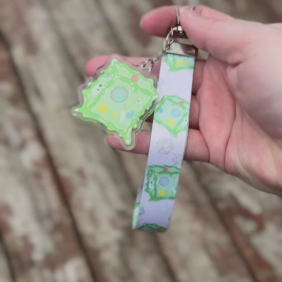 Short video showing a Wiggle Cube or  Gelatinous Cube wristlet. Cubes are green on a tan background with a matching green acrylic charm.